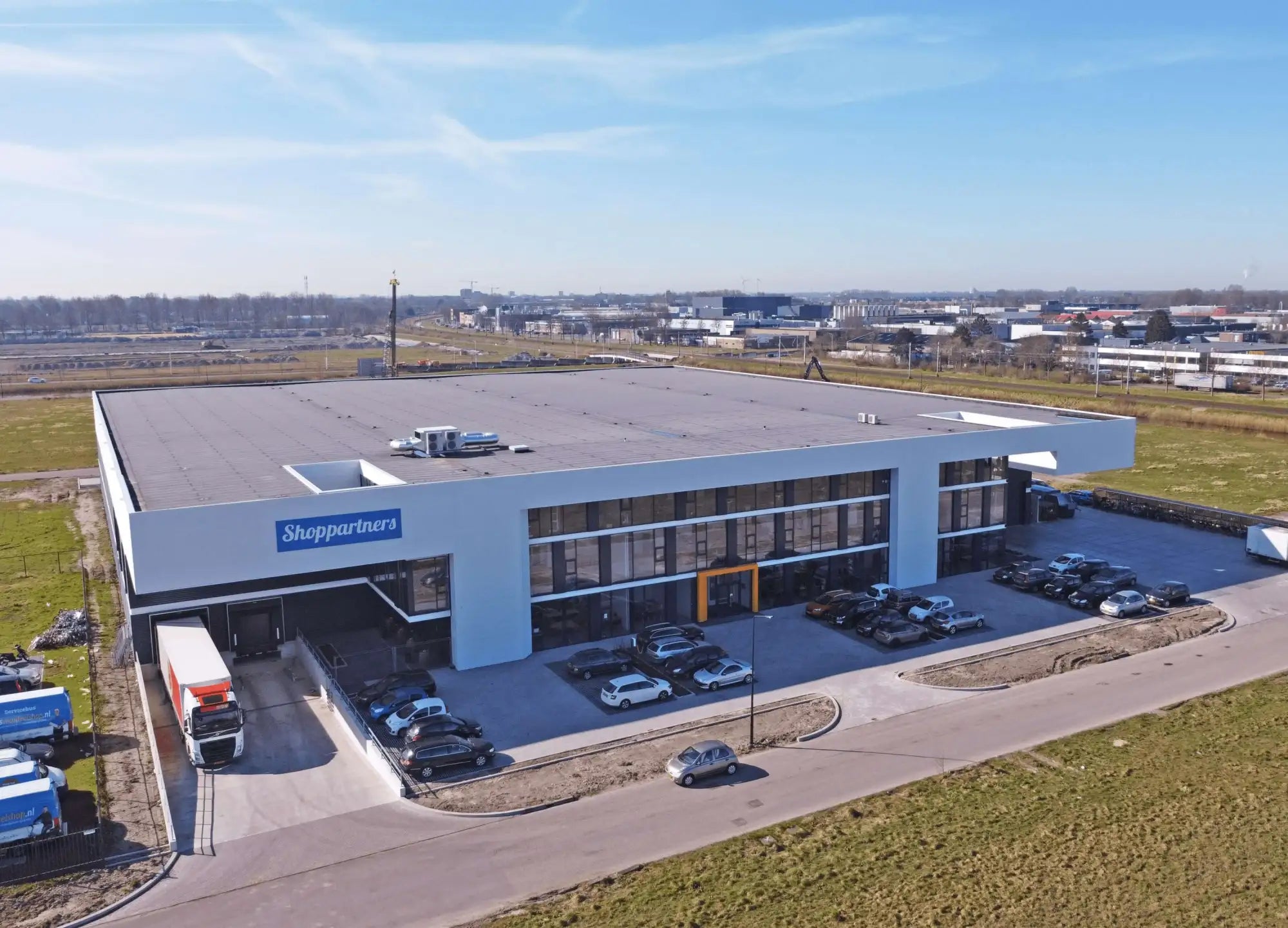 Modern wit en grijs magazijngebouw met een plat dak, grote glazen ramen en het 'shoppartners'-logo op de gevel.